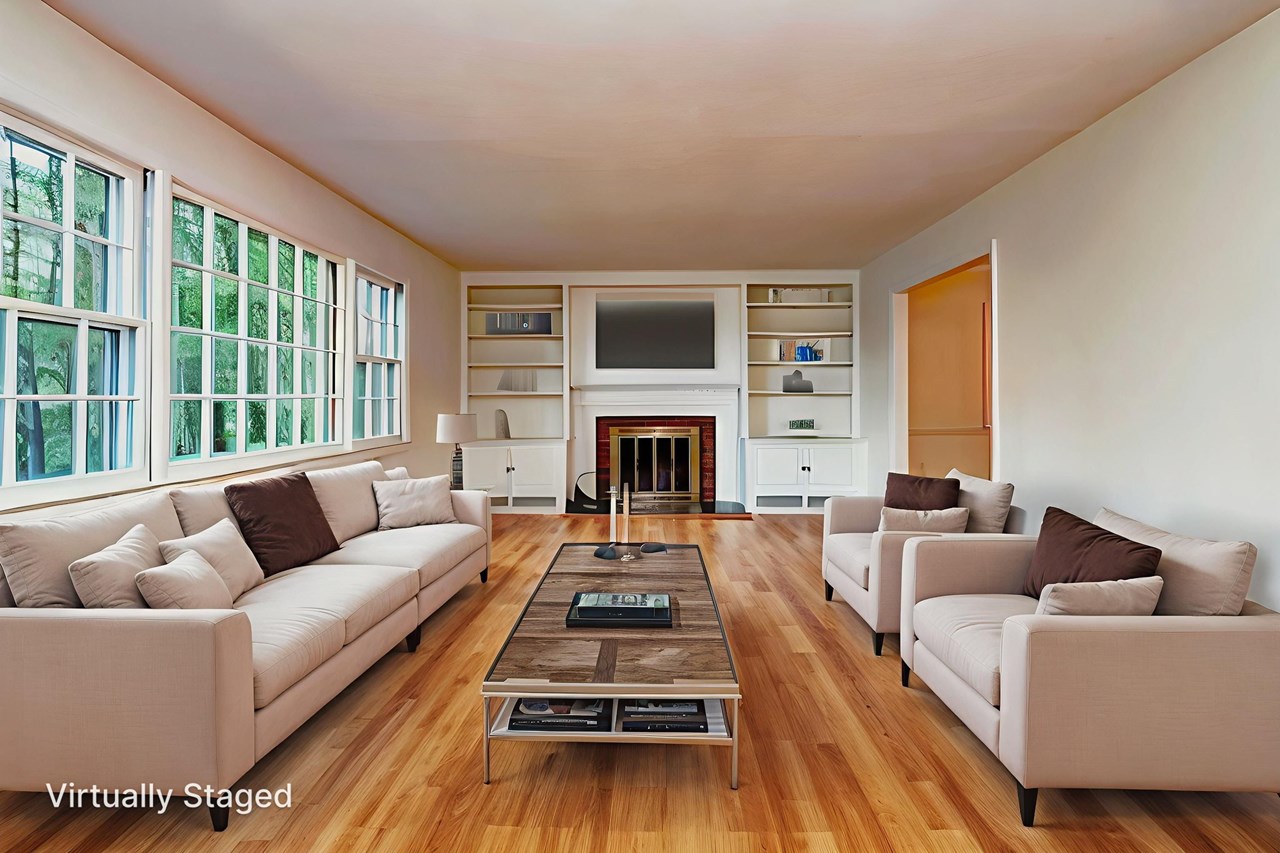 bright and spacious living room with hardwood floors and a cozy fireplace. spacious living room with refinished hardwood floors, a classic wood-burning fireplace, and large windows that fill the space with natural light—perfect for everyday comfort or entertaining guests.